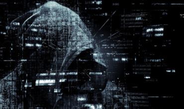 Silhouette of a hooded hacker in a dark digital environment, illustrating cybercrime threats during summer.