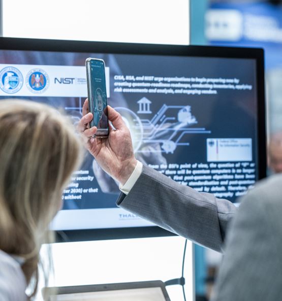 Présentation d’un système de reconnaissance faciale sur smartphone à TRUSTECH, avec une personne tenant un téléphone face à lui et une autre personne regardant l'écran.