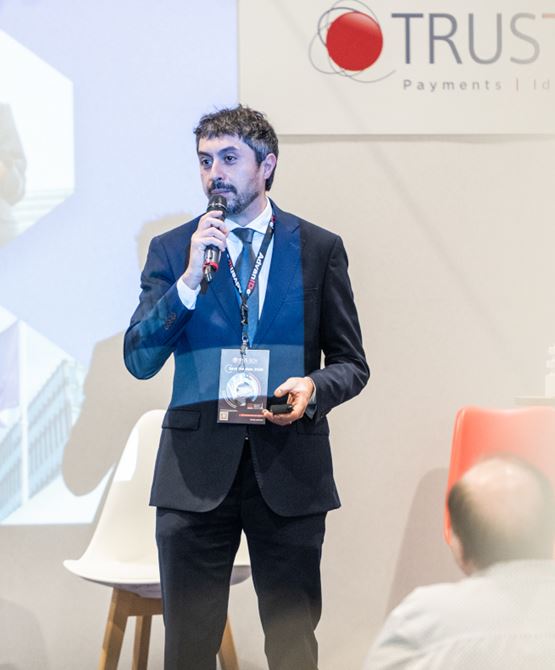 Giuseppe DE MARCO speaking at TRUSTECH 2025, holding an award in his hands.