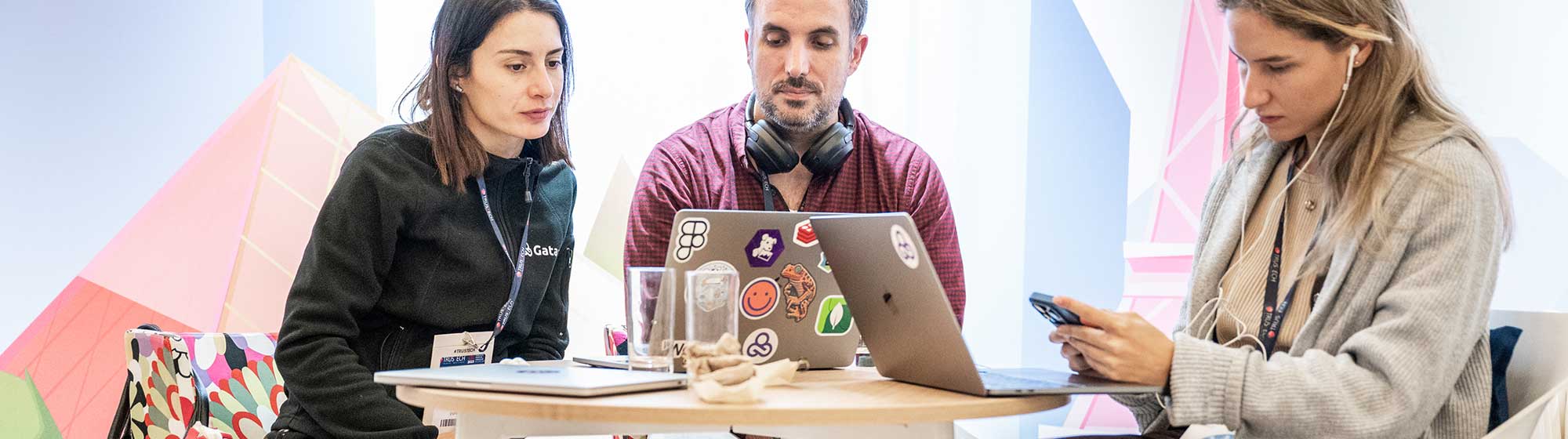 A man and two women sitting at a table working with their laptops and phones