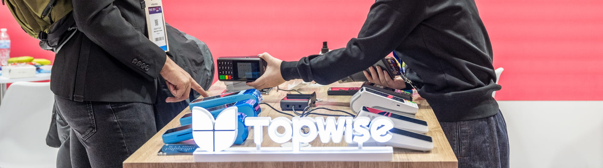 Demonstration of a payment terminal at a booth during TRUSTECH, between an exhibitor and a visitor.