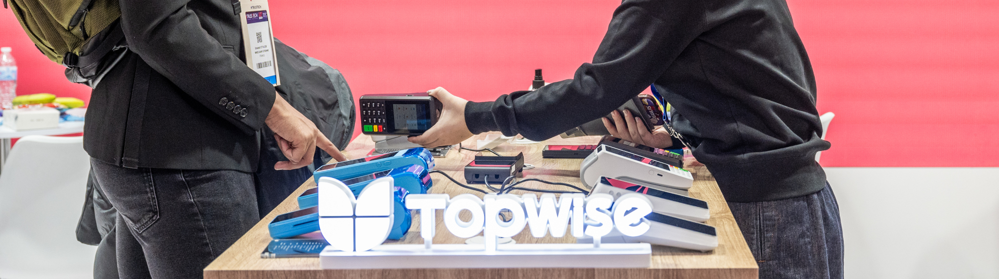 Démonstration d’un terminal de paiement sur un stand lors du salon TRUSTECH, entre une exposante et un visiteur.