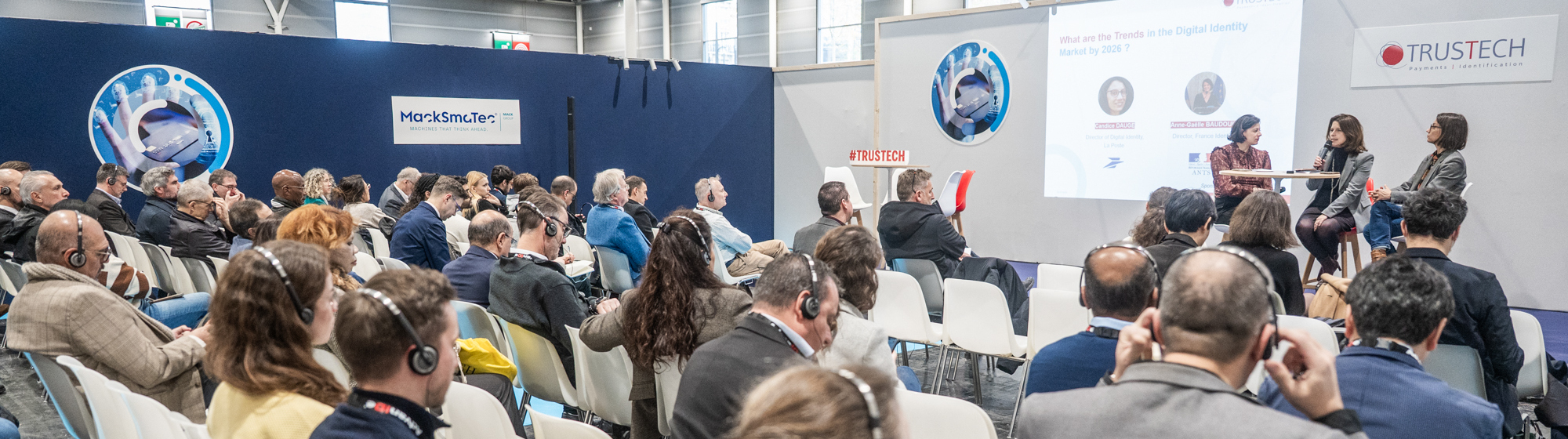 Session de conférence TRUSTECH avec des participants internationaux portant des casques, à l'écoute des experts sur scène