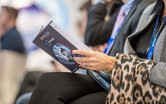 a seated woman flips through the Trustech event catalog