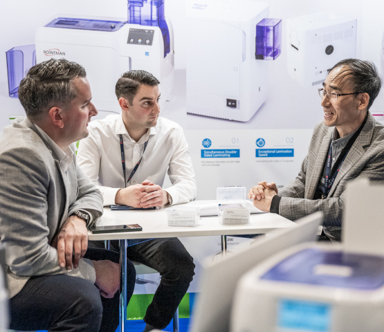 3 visiteurs et exposants en réunion autour d'une table sur un stand TRUSTECH